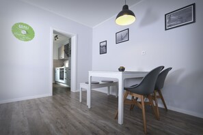 A modern dining area with a white table and chairs, a pendant light, and a clock on the wall.