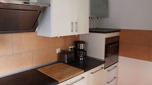 Une cuisine compacte avec des meubles blancs, une hotte de cuisinière en acier inoxydable, une machine  à café et un four à micro-ondes.