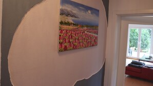 Une pièce avec un grand tableau représentant un paysage, un canapé rouge et une vue sur l’extérieur par une fenêtre.
