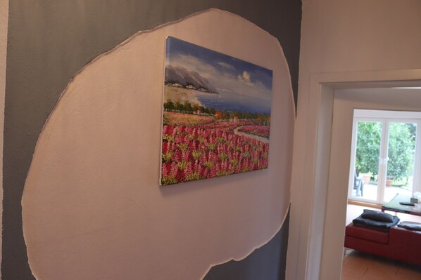 A room with a large painting of a landscape, a red sofa, and a view of the outdoors through a window.