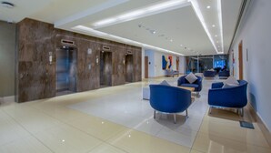 Eine moderne Lobby mit einer Marmorrezeption, Aufzügen und einer blauen Sitzgelegenheit.