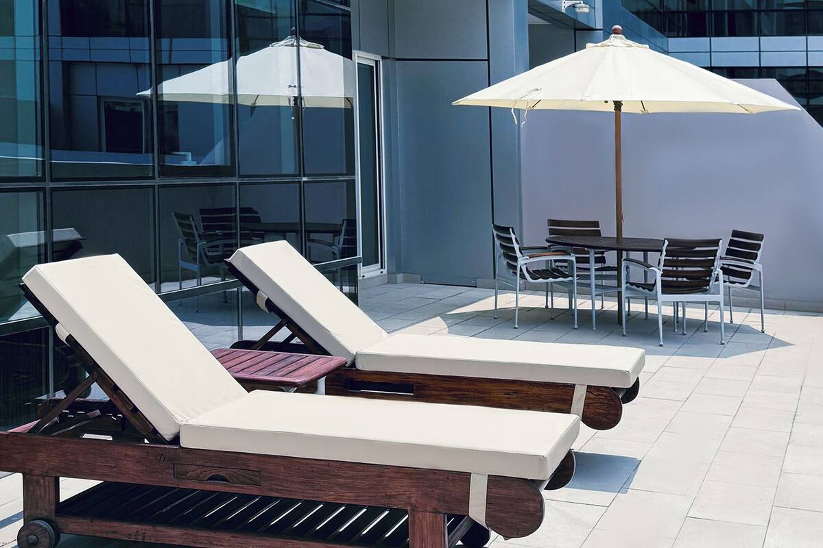 Terrassenstühle und Sonnenschirme auf einer gefliesten Terrasse, im Hintergrund ein modernes Gebäude.
