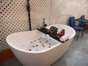 Una bañera con pétalos de rosa, una vela y artículos de aseo en una bandeja.