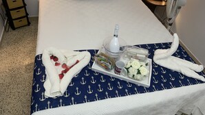 Una cama bien hecha con sábanas blancas, una colcha de rayas azules y blancas con motivos de ancla, un recipiente con artículos de aseo y una botella de agua.