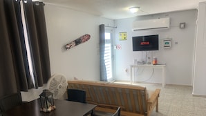 Una sala de estar con un banco de madera, una mesa de comedor con sillas, un televisor y un ventilador.