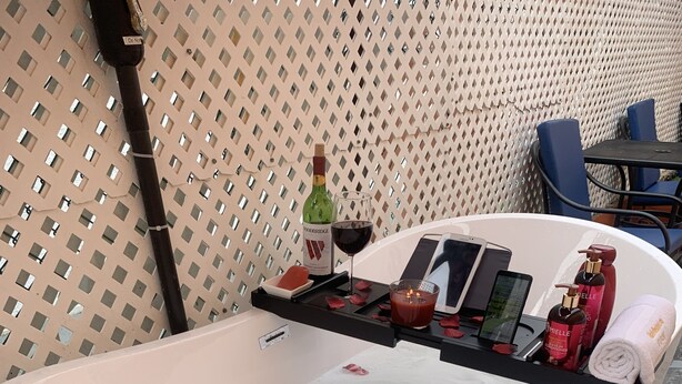 Una bañera con pétalos de rosa, una botella de vino y artículos de tocador.