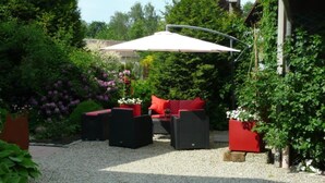 Un patio al aire libre con un paraguas blanco, muebles de mimbre negro y cojines rojos.
