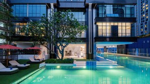 Un hotel moderno con piscina, sillones de descanso y una entrada bien iluminada.