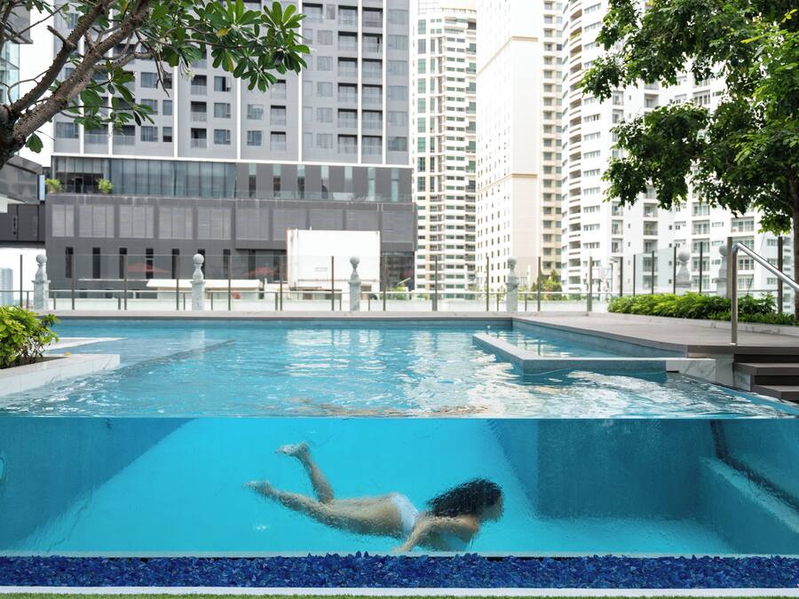 A swimming pool with a person swimming, surrounded by tall buildings and greenery.