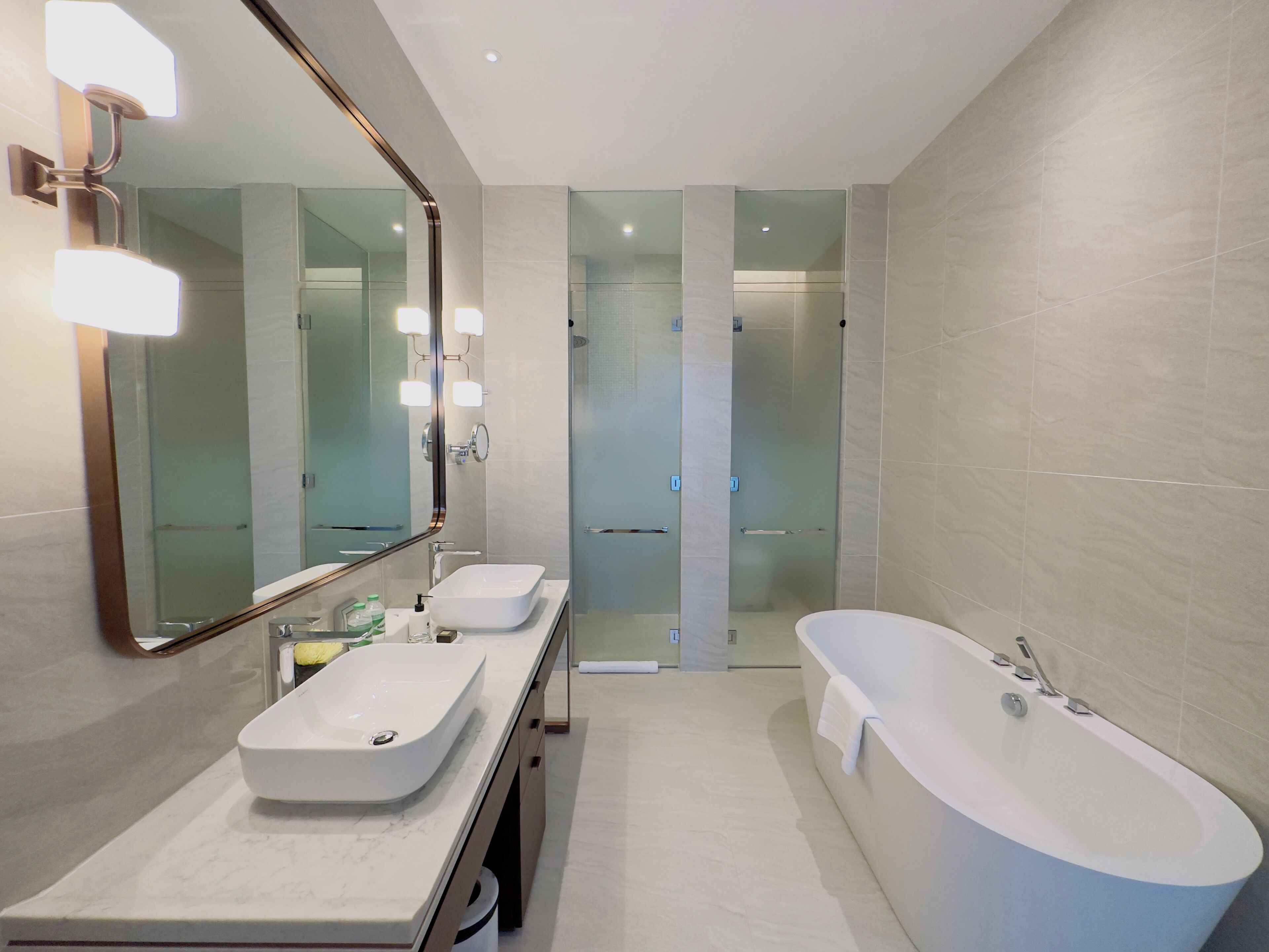 A modern bathroom with a large mirror, two sinks, a bathtub, and a glass shower enclosure.