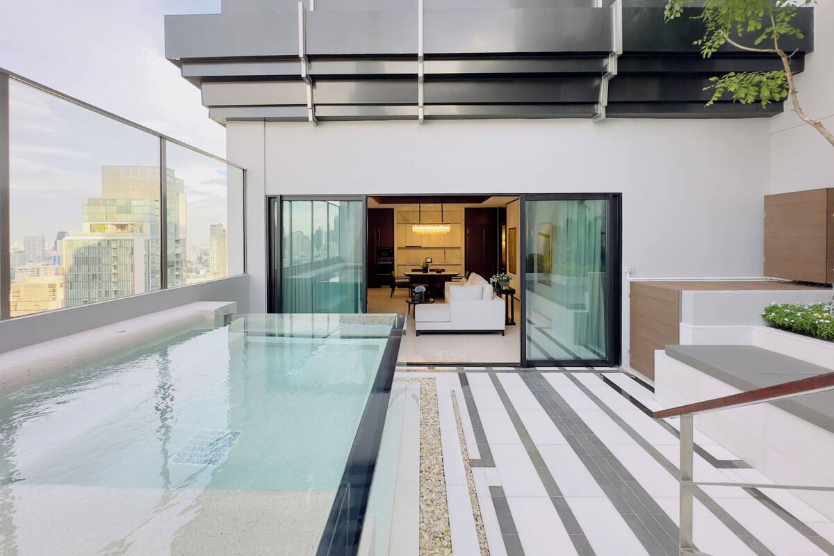 A modern rooftop pool with a city view, a glass-enclosed kitchen, and a minimalist living area.