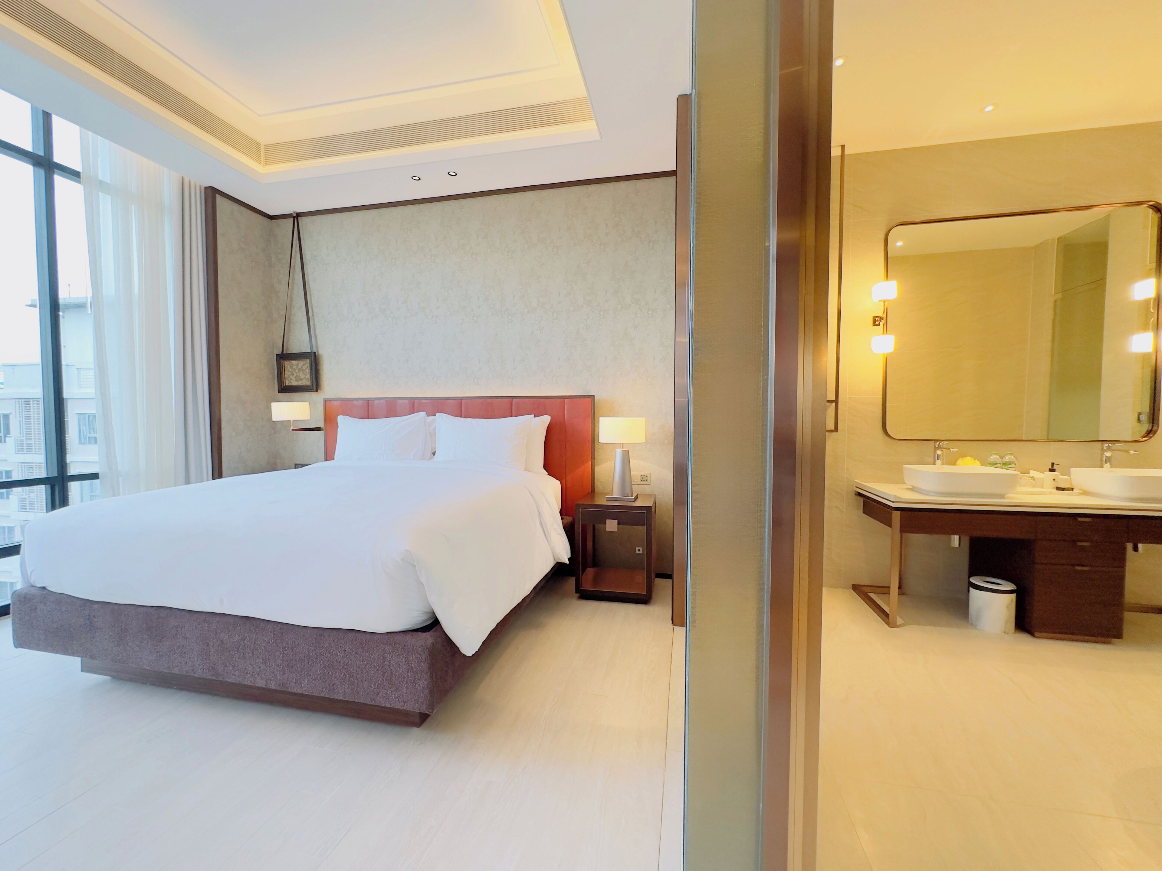 A hotel room with a large bed, a bathroom with a mirror, and a view of the city.