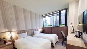 Habitación de hotel con dos camas, un escritorio, una silla, un televisor y una ventana con vistas a la ciudad.