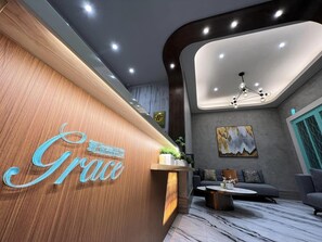 A reception area with a wooden reception desk, a modern chandelier, and a grey sofa. - GRACE HOTEL DUNBEI (Taipei)