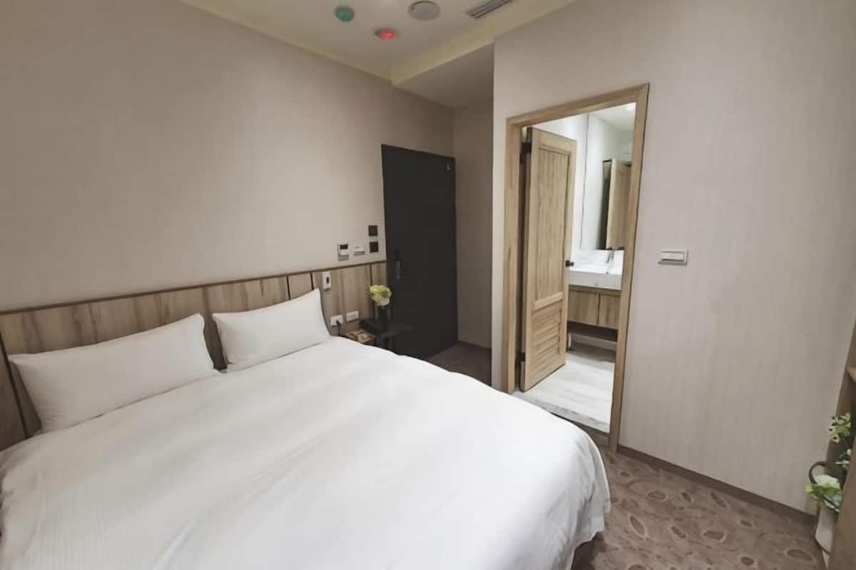 Quarto de hotel com uma cama, mesa de cabeceira, espelho, porta que dá para um banheiro e uma pequena planta.