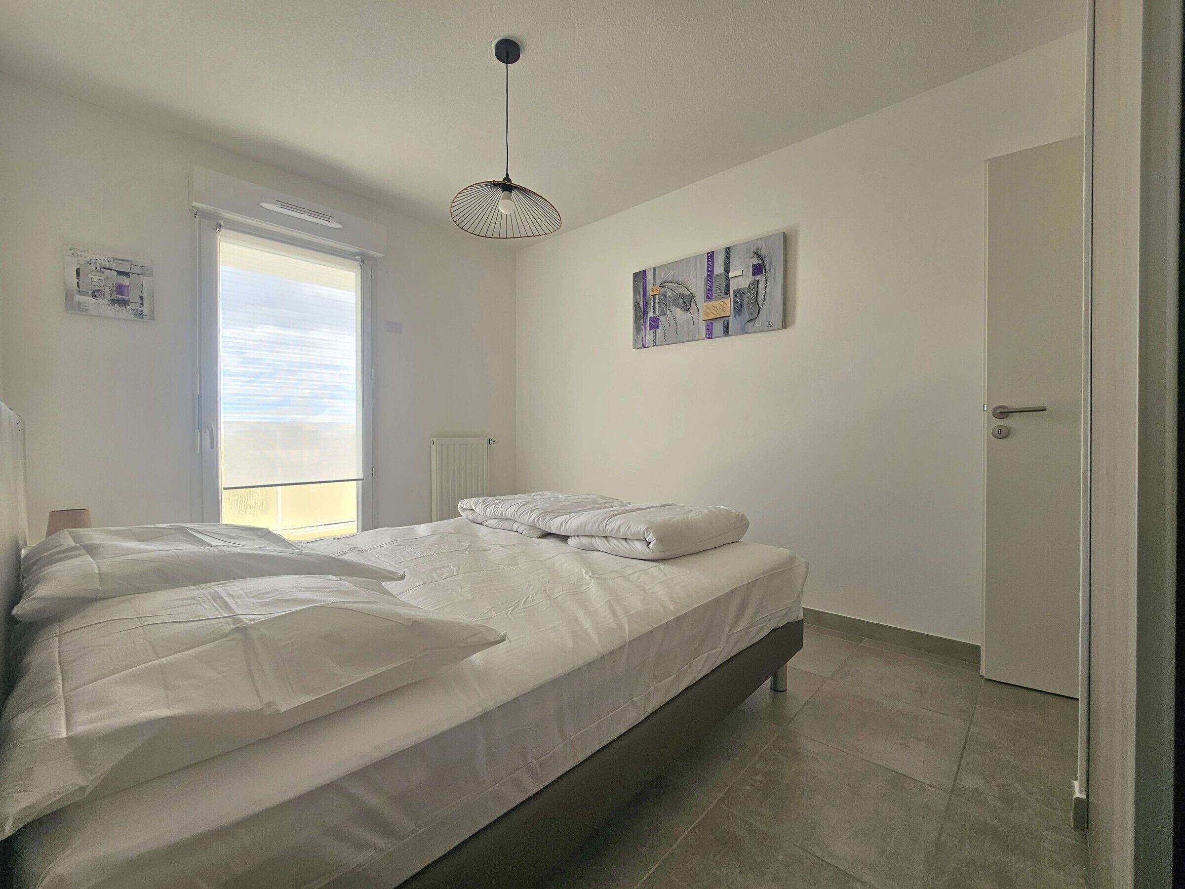 A bedroom with a bed, a radiator, a door, and a window.