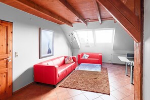 Une pièce avec un canapé rouge, un tapis marron, un radiateur blanc et une fenêtre donnant sur un beau paysage.