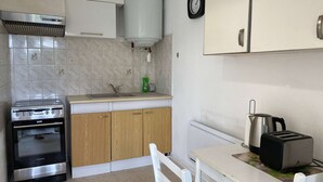 A kitchen with a built-in oven, a sink, wooden cabinets, a white countertop, a kettle, and a toaster. - Bright 1-Bed Apt near Thermal Baths, Equip’d Kitchen, WiFi, Parking, 2-Star Rated, 45m² (Balaruc-les-Bains)