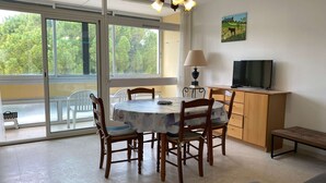 A dining area with a round table, wooden chairs, a lamp, and a television on a wooden cabinet. - Bright 1-Bed Apt near Thermal Baths, Equip’d Kitchen, WiFi, Parking, 2-Star Rated, 45m² (Balaruc-les-Bains)