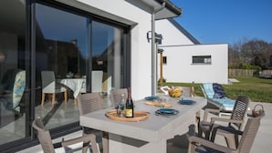 Een buiten eethoek met een tafel voor vier personen, omringd door stoelen, en een glazen deur die leidt naar een binnenruimte.