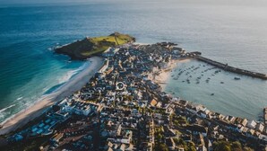 An aerial view of a coastal town with a beach, a pier, and a densely packed residential area.