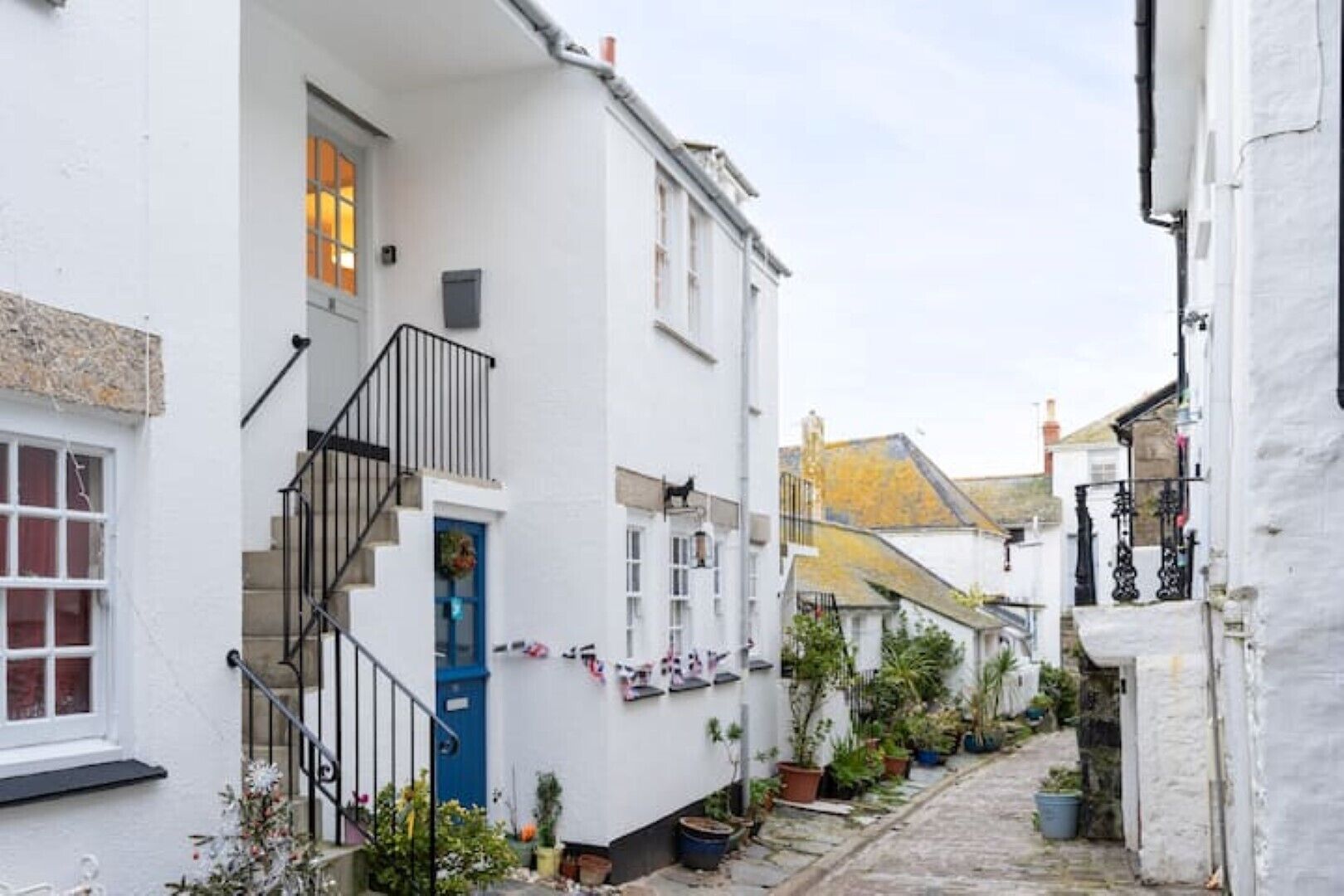A narrow street with white buildings, a blue door, and a staircase leading to the entrance.