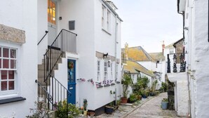 A narrow street with white buildings, a blue door, and a staircase leading to the entrance.
