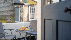 A balcony with a table set for breakfast, a chair, and a door leading to a building with a stone facade.