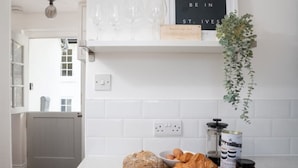 A kitchen with white tiles, a loaf of bread, croissants, jars of spreads, and a hanging plant.