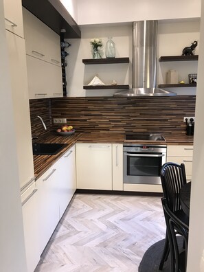 A modern kitchen with wooden accents, a stainless steel range hood, and a dining area with a black chair.