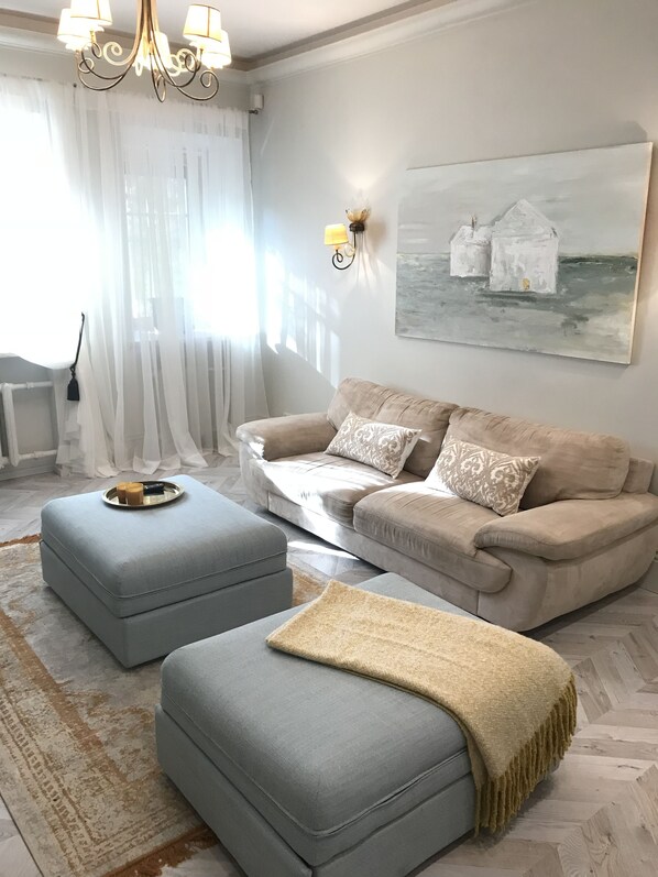 A living room with a beige sofa, two grey ottomans, a coffee table, and a painting on the wall.
