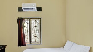 Een kamer met een bed, een raam met decoratief rooster en een airconditioner aan de muur.