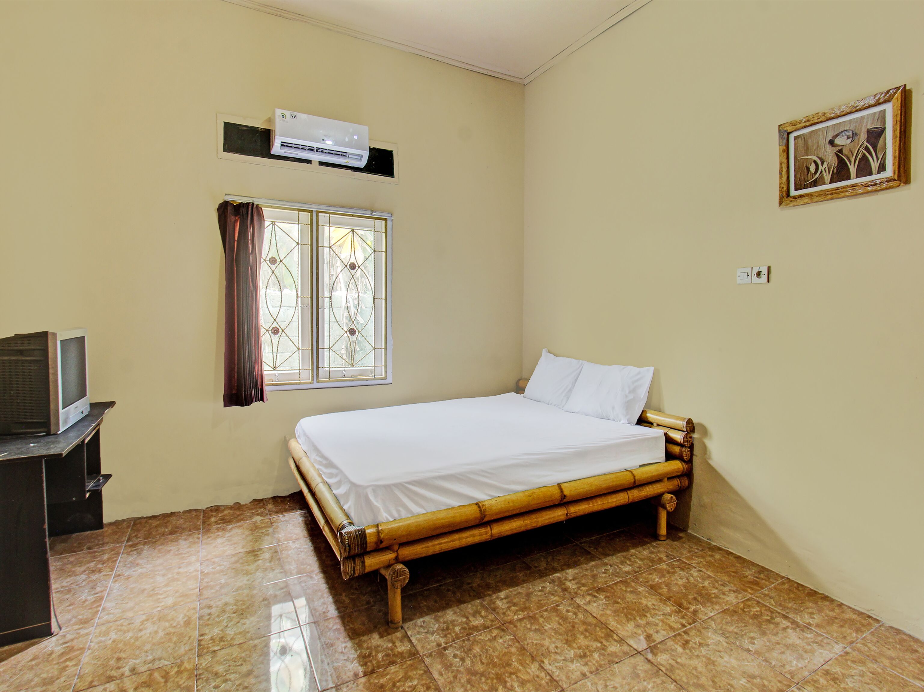 A room with a bed, a television on a stand, a window with curtains, and an air conditioner on the wall.