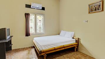 A room with a bed, a television on a stand, a window with curtains, and an air conditioner on the wall.