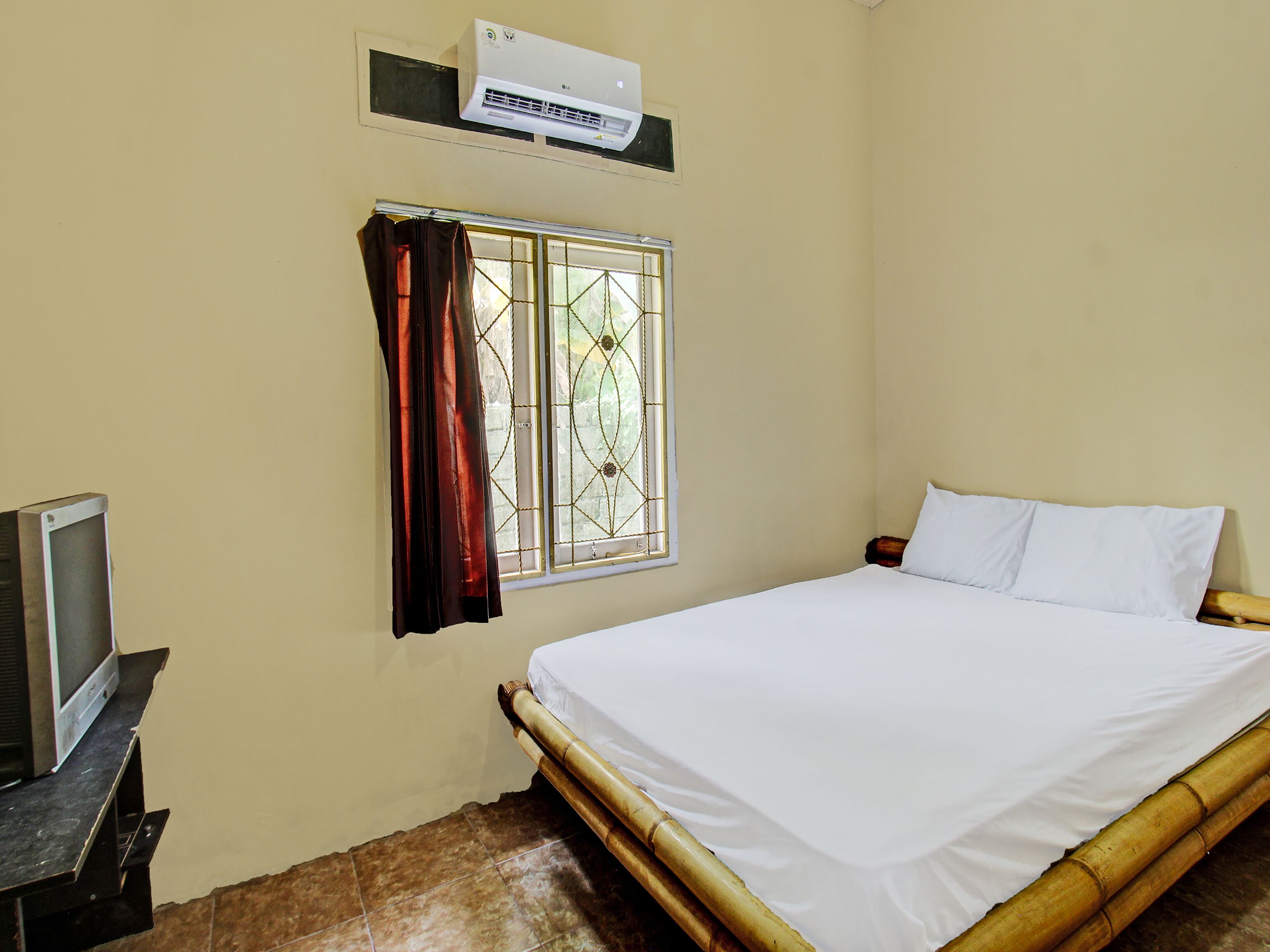 A room with a bed, a TV on a stand, a window with curtains, and an air conditioner mounted on the wall.