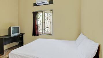 Una habitación con cama, un escritorio con televisor, una ventana con rejas y un equipo de aire acondicionado en la pared.