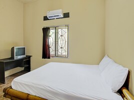 Una habitación con cama, un escritorio con televisor, una ventana con rejas y un equipo de aire acondicionado en la pared.