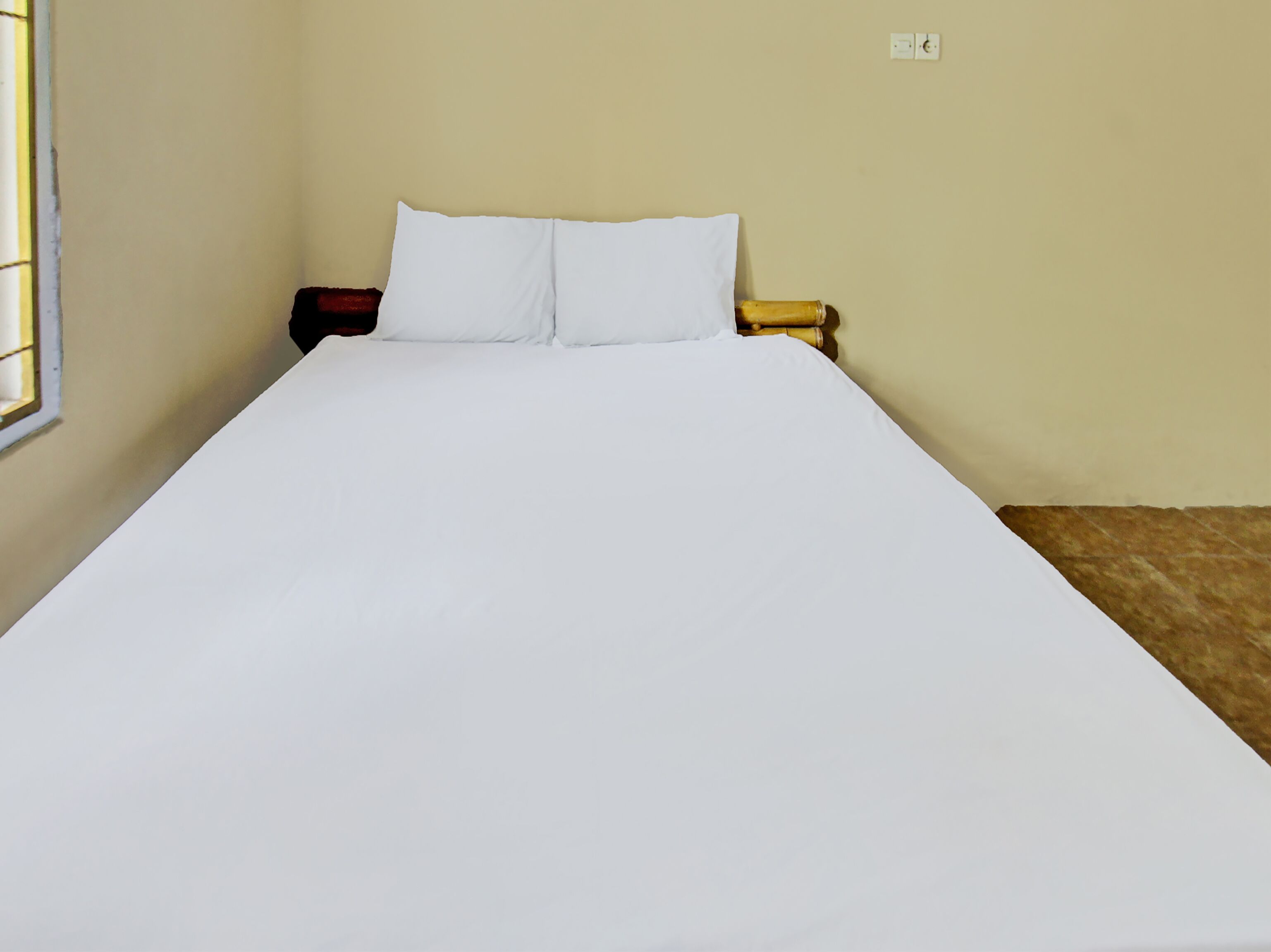 A single bed with white bedding in a room with beige walls and a window on the left.