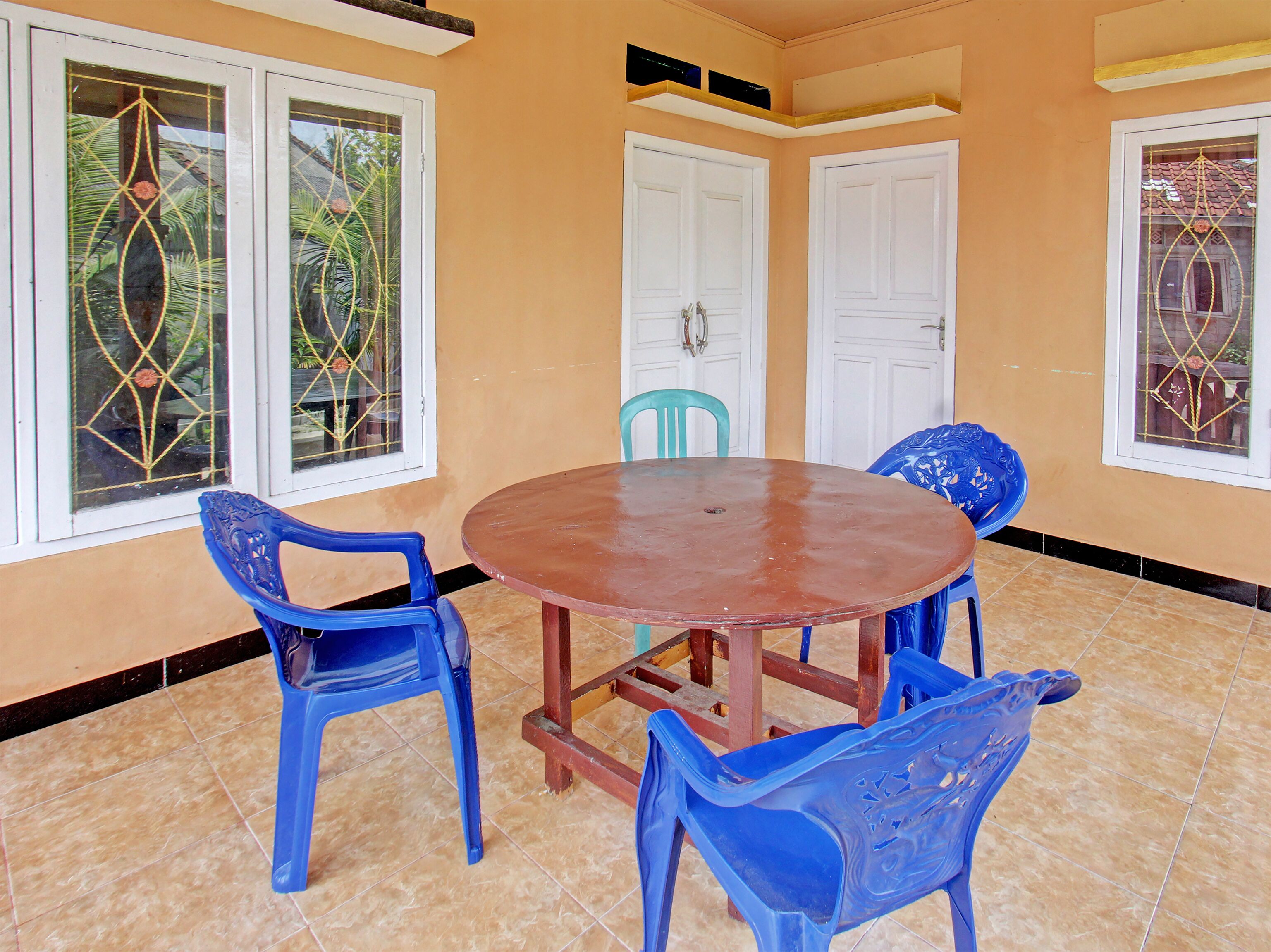 A room with a round wooden table surrounded by blue plastic chairs, white doors, and windows with decorative glass.
