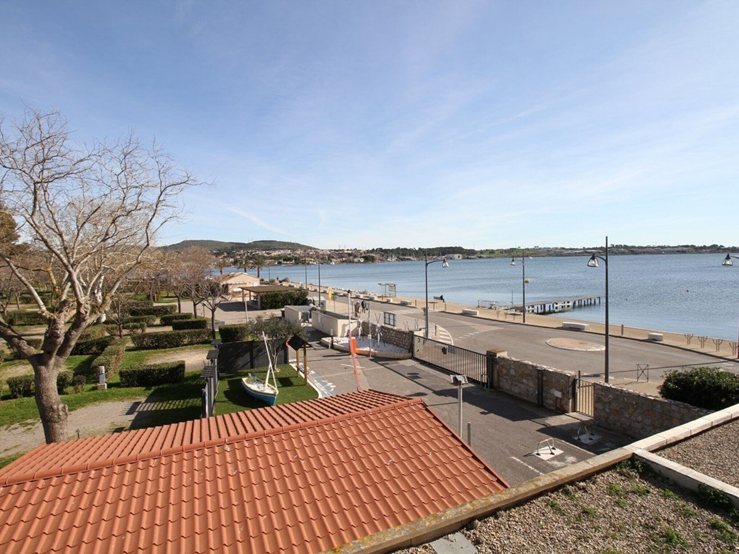 A coastal marina with a clear view of the water, a parking area, and a building with a red-tiled roof.