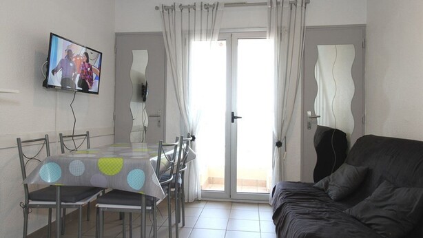A dining area with a table and chairs, a television mounted on the wall, and a sliding glass door leading to an outdoor area. - Charming Mezzanine T1, A/C, Thau View (Balaruc-les-Bains)