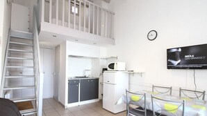 A compact living space with a kitchenette, dining area, and a TV mounted on the wall. - Charming Mezzanine T1, A/C, Thau View (Balaruc-les-Bains)
