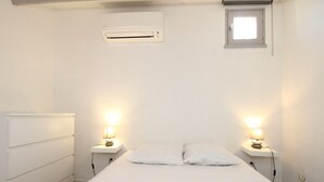 A bedroom with a bed, two bedside tables with lamps, a dresser, an air conditioning unit, and a small window. - Charming Mezzanine T1, A/C, Thau View (Balaruc-les-Bains)