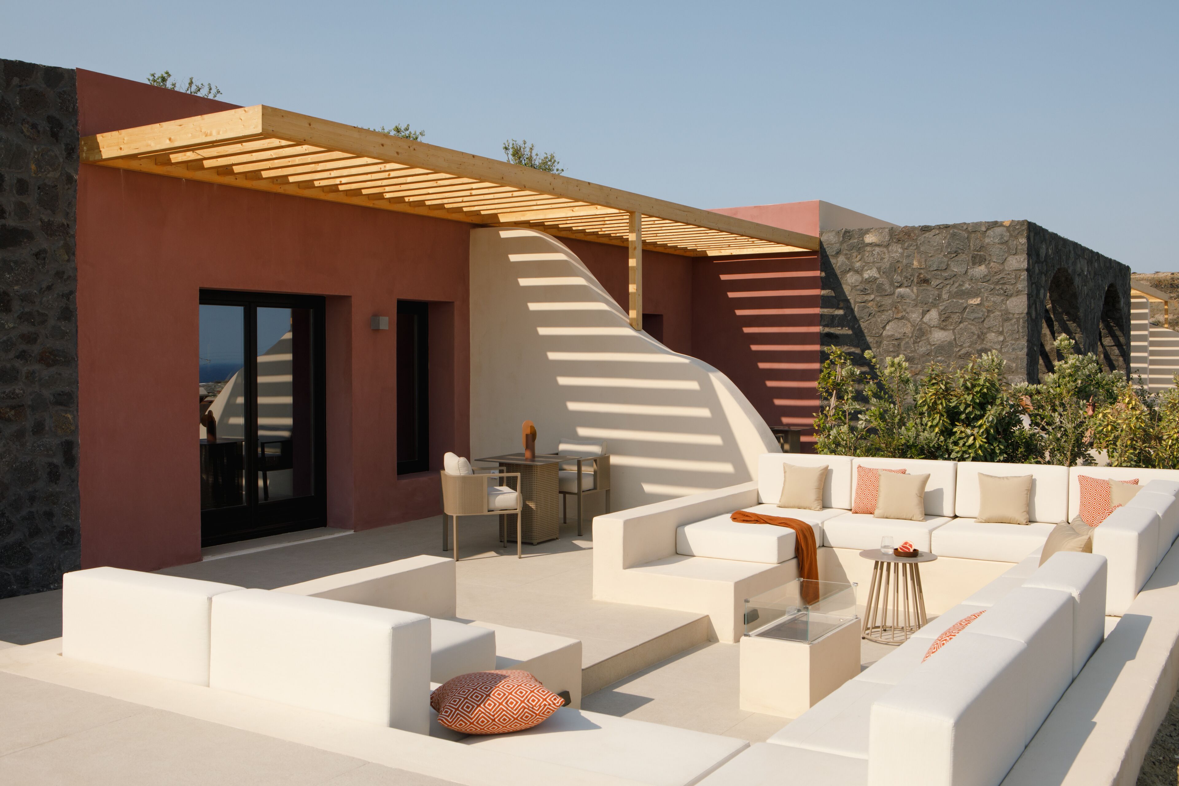 A modern outdoor seating area with white sofas and a wooden pergola.