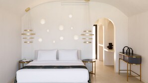 A modern hotel room with a large bed, bedside tables, a round table, and a decorative hanging light fixture. - Elysian Retreat - Adults Only (Santorini)
