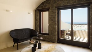 A modern room with a black sofa, a small round table, and a large window with a view of the beach. - Elysian Retreat - Adults Only (Santorini)