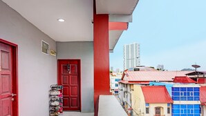 Ein Balkon mit einer roten Tür, einem Schuhregal und Blick auf farbenfrohe Gebäude im Hintergrund.