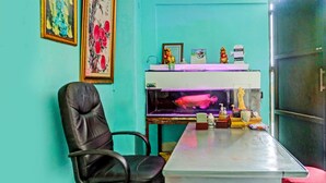 Ein Zimmer mit türkisfarbenen Wänden, einem schwarzen Bürostuhl, einem Schreibtisch mit Aquarium und einem Kühlschrank.