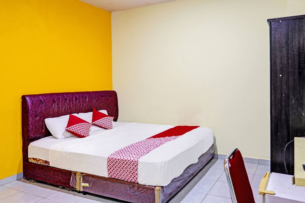 A single bed with a red headboard and white bedding, a chair, and a small table in a room with yellow and white walls.