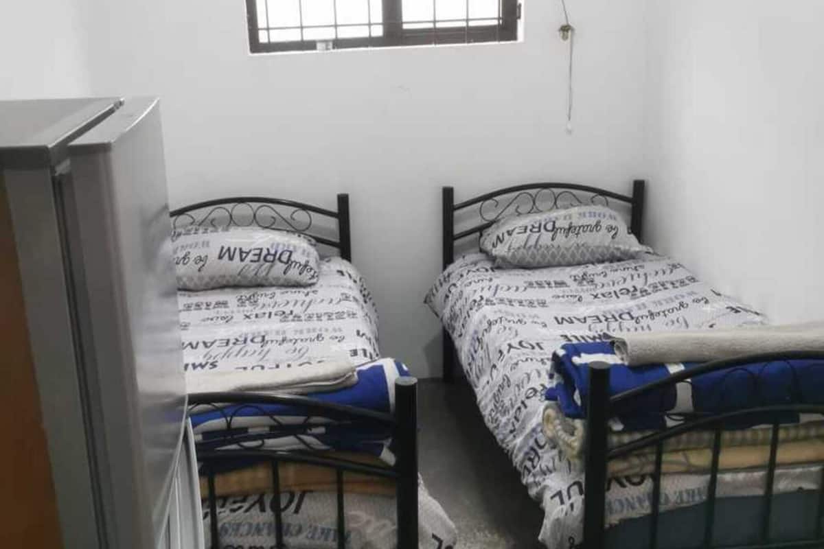 A small, sparsely furnished room with two single beds, a window with a curtain, and a television on a stand.